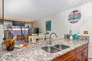A kitchen with a double sink, a view of the ocean, a painting, and a clock on the wall. - Kona Reef F22: Top-Floor Condo with Ocean Views (Kailua-Kona)