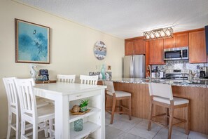 Gather around the cozy dining table or belly up to the breakfast bar, where morning coffee and sunset views blend seamlessly in this bright, coastal-inspired kitchen space. - Kona Reef F22: Top-Floor Condo with Ocean Views (Kailua-Kona)