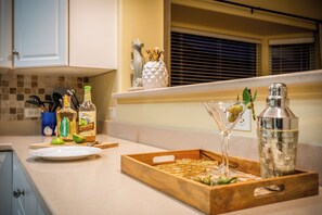 A kitchen counter with a wooden tray holding cocktail glasses, a martini glass, and a bottle. - Hale Kona: Home - Ocean Views/Hot Tub/Private Yard (Kailua-Kona)