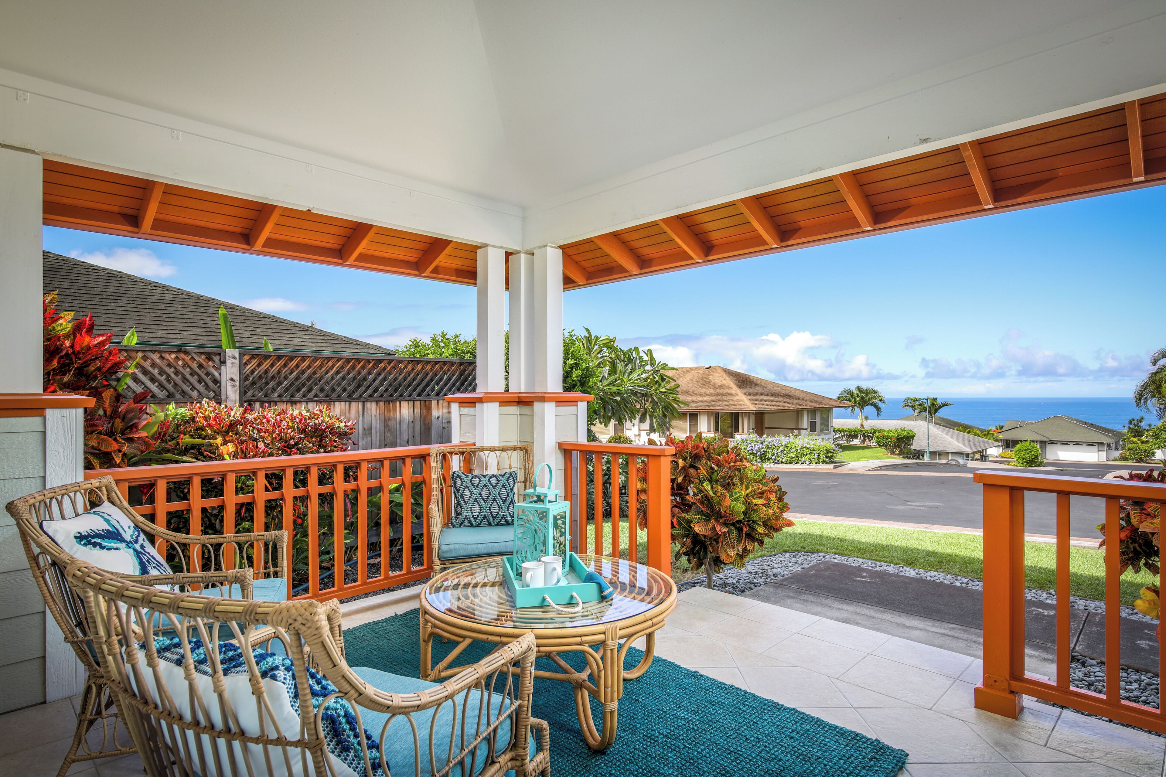 A covered outdoor seating area with wicker furniture and a view of the ocean.