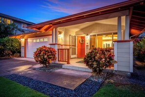 A residential house with a garage, a covered porch, and a well-maintained front yard with decorative shrubs. - Hale Kona: Home - Ocean Views/Hot Tub/Private Yard (Kailua-Kona)