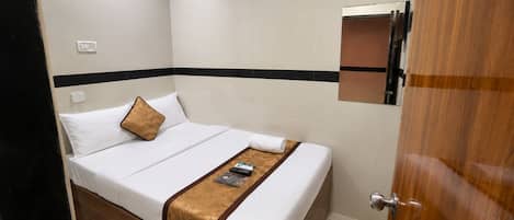Una habitación de hotel con cama, mesita de noche, espejo y puerta.