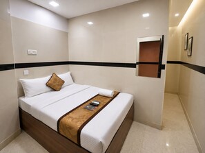 A hotel room with a bed, a bedside table, a remote control, and a wall-mounted shelf. - Angel Inn By Glitz Hotels (Mumbai)