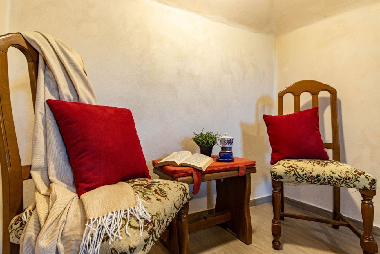 Deux chaises en bois avec des coussins rouges, une petite table sur laquelle se trouvent un livre et une théière, et une plante.