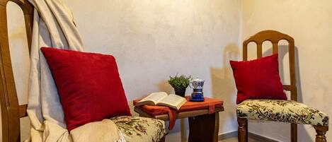 Deux chaises en bois avec des coussins rouges, une petite table sur laquelle se trouvent un livre et une théière, et une plante.