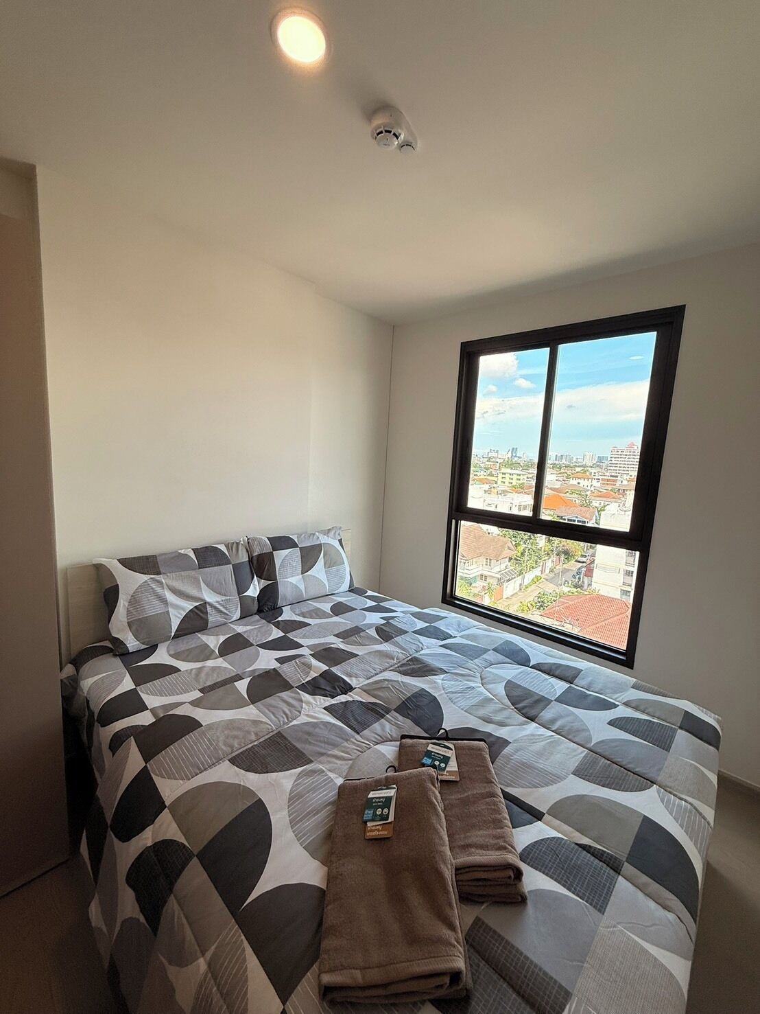 A hotel room with a large bed, a window with a city view, and a ceiling light.