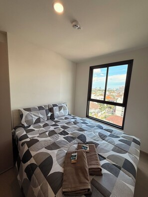 Habitación de hotel con una cama grande, una ventana con vista a la ciudad y una lámpara en el techo.