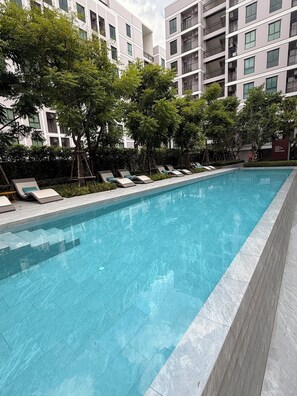 Una piscina con sillas de descanso y árboles, rodeada por un edificio con varios pisos y balcones.