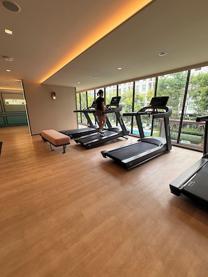 A gym with treadmills, a bench, and large windows offering a view of the outdoors. - Cozy 1-bedroom apartment in fabulous Bang Chak area with AC (Krung Thep Maha Nakhon)