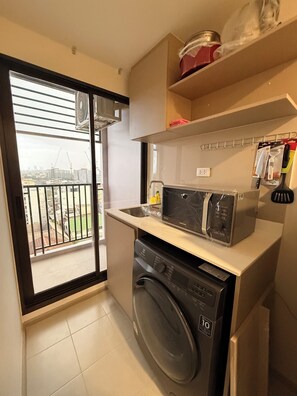 A compact kitchen with a washing machine, a microwave, and a small sink. - Cozy 1-bedroom apartment in fabulous Bang Chak area with AC (Krung Thep Maha Nakhon)