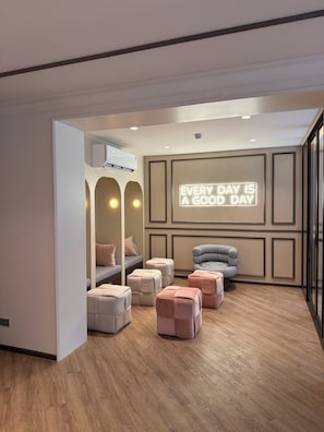 Ein modernes Zimmer mit einer Couch, Poufs, einem Sessel und einem motivierenden Spruch an der Wand.