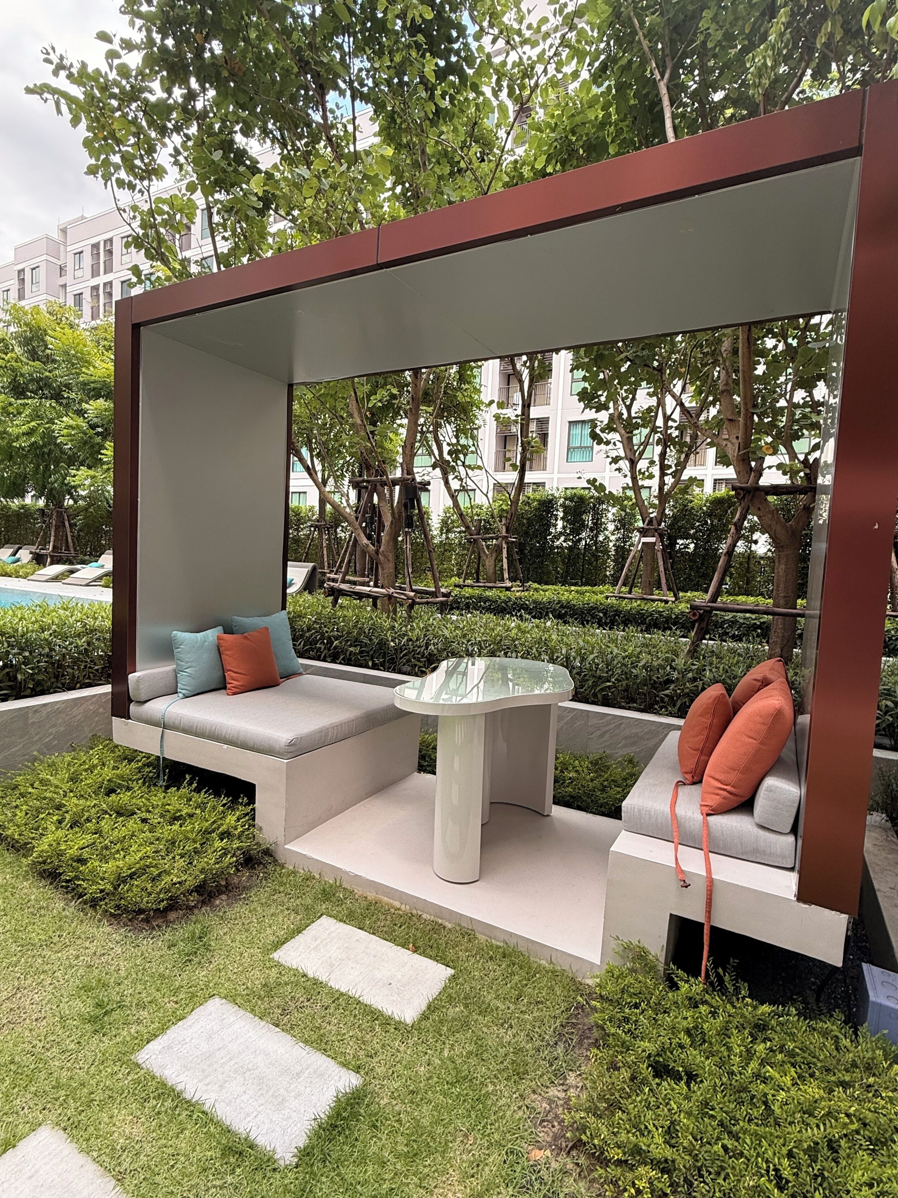 A modern outdoor seating area with a glass-top table, cushioned benches, and a clear view of the surrounding greenery and buildings.