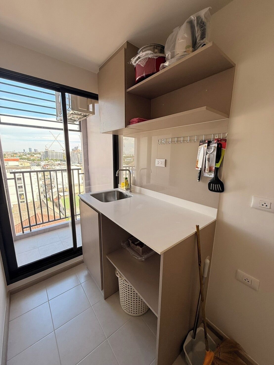 A small kitchen with a sink, a drying rack, and a view of the city through a balcony.