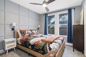 Une chambre à coucher comprenant un lit, des tables de chevet, un ventilateur de plafond, une fenêtre avec des rideaux et une armoire en bois.