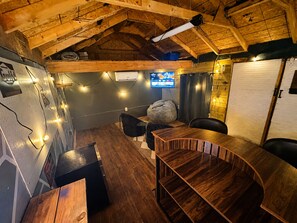 Tunnelmallinen huone, jossa on puinen katto, seinälle asennettu televisio sekä oleskelualue, jossa on pöytä ja tuolit.