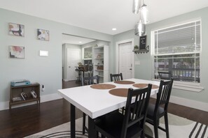Un coin repas avec une table blanche, quatre chaises et un luminaire suspendu au design moderne.