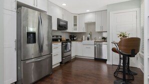 A modern kitchen with stainless steel appliances, white cabinetry, and a wooden dining area. - Boho Bliss Downtown Retreat - Tampa Heights -Tampa (Tampa)