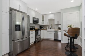 A modern kitchen with stainless steel appliances, white cabinetry, and a wooden dining area. - Boho Bliss Downtown Retreat - Tampa Heights -Tampa (Tampa)