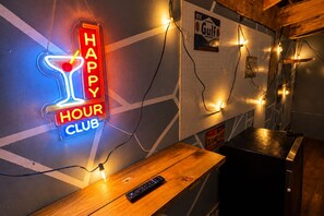 A neon sign reading 'HAPPY HOUR CLUB' on a wall, a wooden table with a remote control, and a pegboard with various items and lights. - Boho Bliss Downtown Retreat - Tampa Heights -Tampa (Tampa)