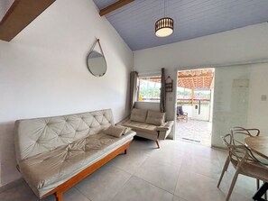 Ein Wohnzimmer mit einer Couch, einem Esstisch mit Stühlen, einer Pendelleuchte und Blick durch ein Fenster.
