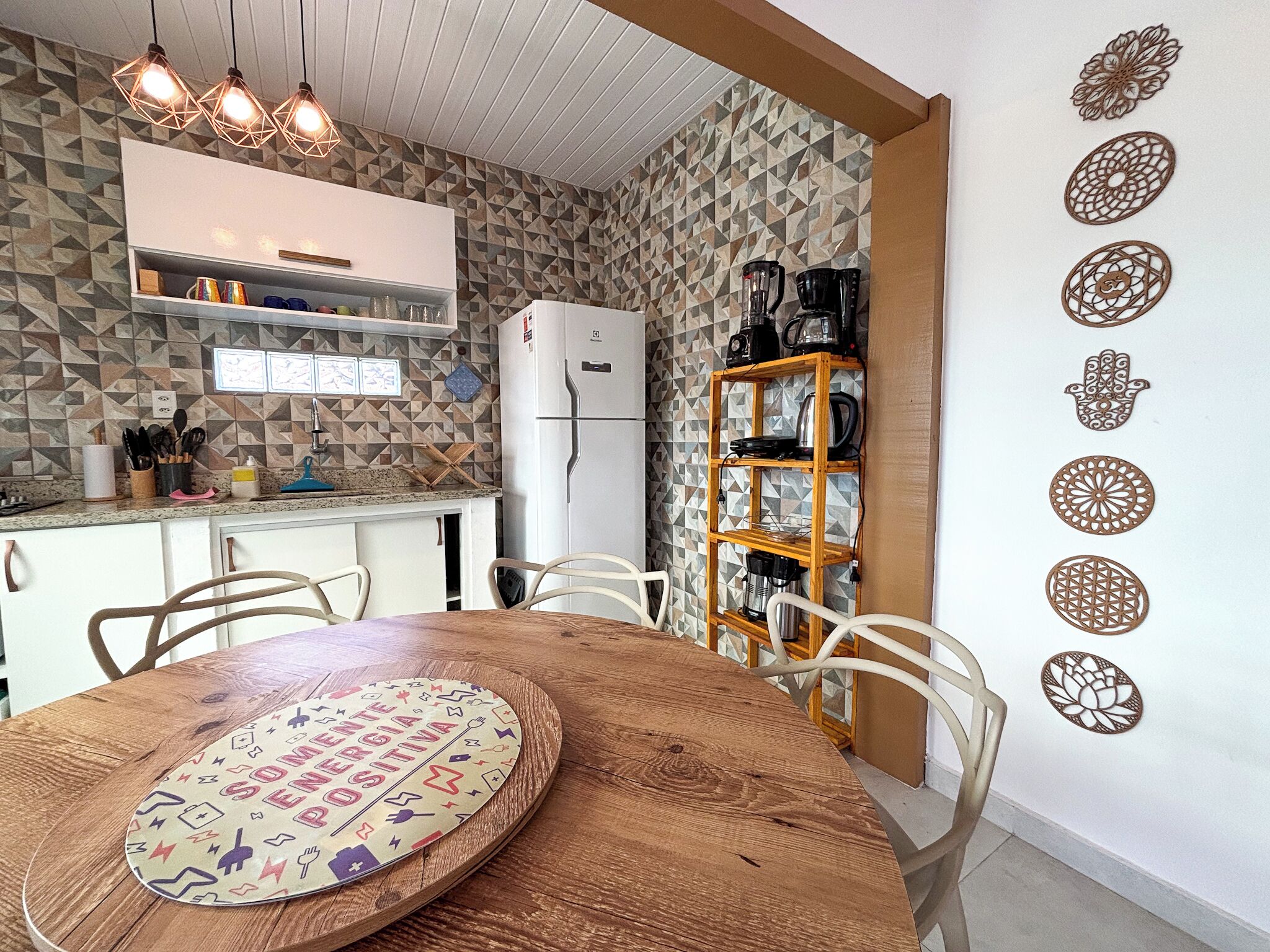 A kitchen with a white refrigerator, a wooden dining table with chairs, and a wall with geometric patterned tiles.