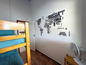 Ein Zimmer mit Etagenbett, einer Wandkarte und einem Standventilator.