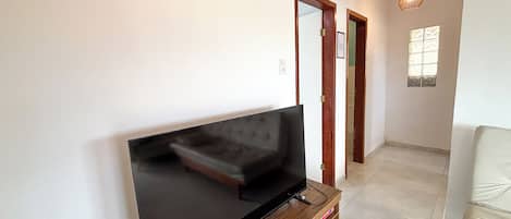 A living room with a flat-screen TV on a wooden stand, a sofa, and a pendant light.