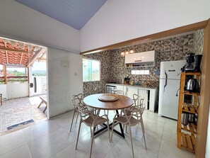 A modern kitchen with a dining area, stone wall backsplash, and a view through an open door. - Casa Silandia Tartaruga, beaches, markets and city center within walking distance; excellent location. (Armação dos Búzios)