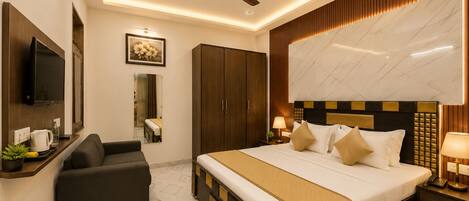 A hotel room with a bed, a sofa, a television, a ceiling fan, and a large mirror.