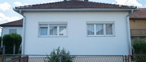 A two-story house with a white exterior, a tiled roof, and a chain-link fence in the foreground.