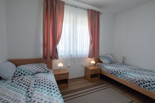 Une chambre avec deux lits, une fenêtre avec des rideaux, des lampes de chevet et un tapis à rayures.
