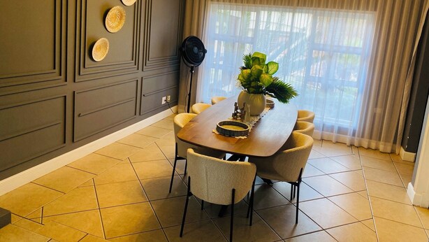 A dining area with a round table, chairs, a fan, and a plant.