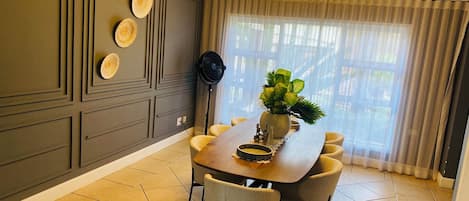 Un comedor con una mesa redonda, sillas, un ventilador y una planta.