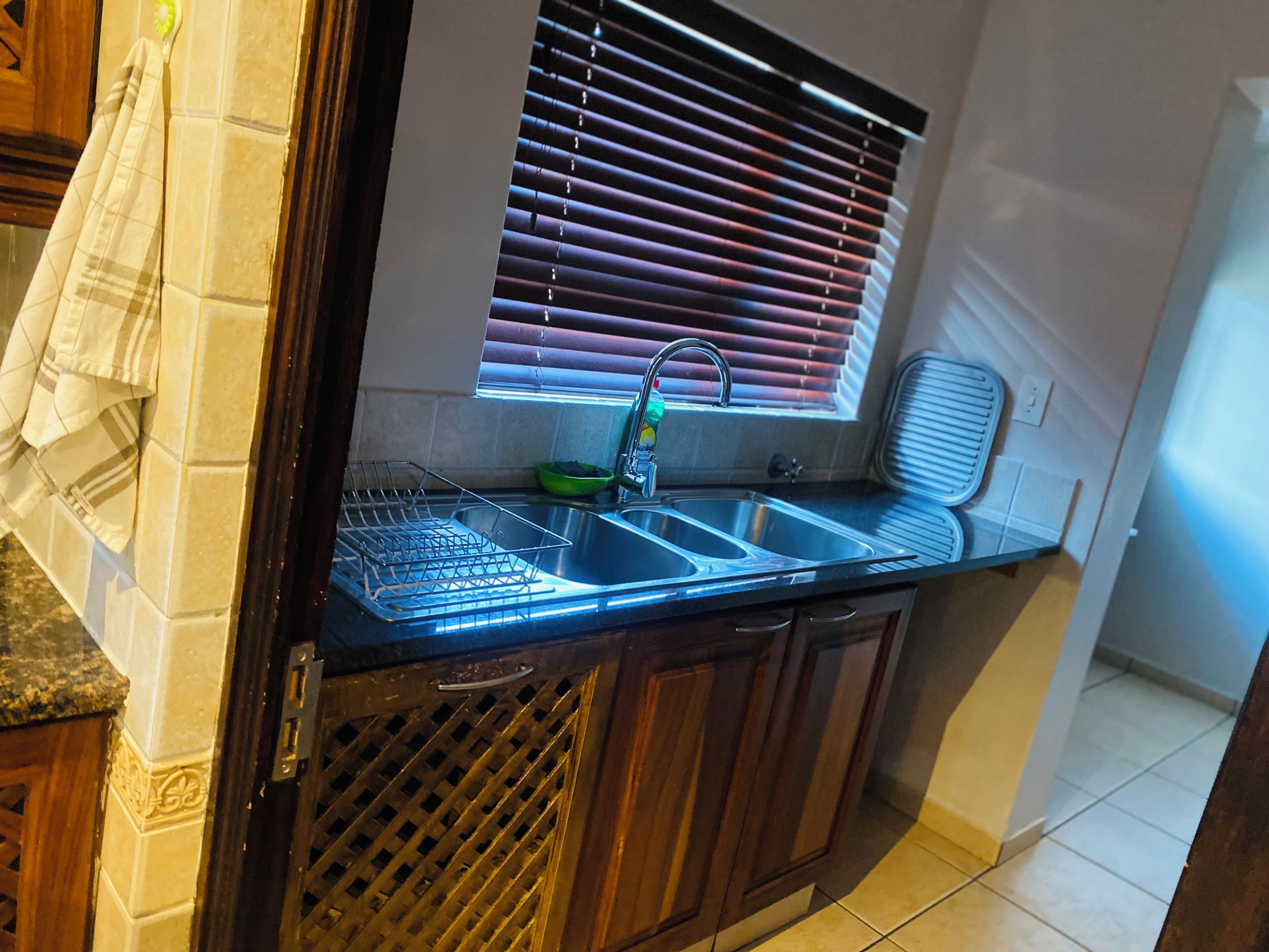 A kitchen with a double sink, a window with blinds, a dish rack, and a towel hanging on the wall.