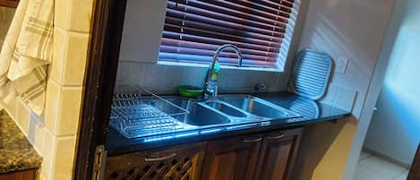 A kitchen with a double sink, a window with blinds, a dish rack, and a towel hanging on the wall.