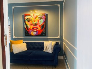 Una habitación con un sofá azul, un almohadón mullido blanco, un cojín decorativo y un cuadro abstracto colorido en la pared.