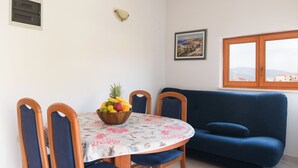Zona de menjador amb taula rodona, cadires, un bol de fruita, un sofà, una finestra i un quadre a la paret.