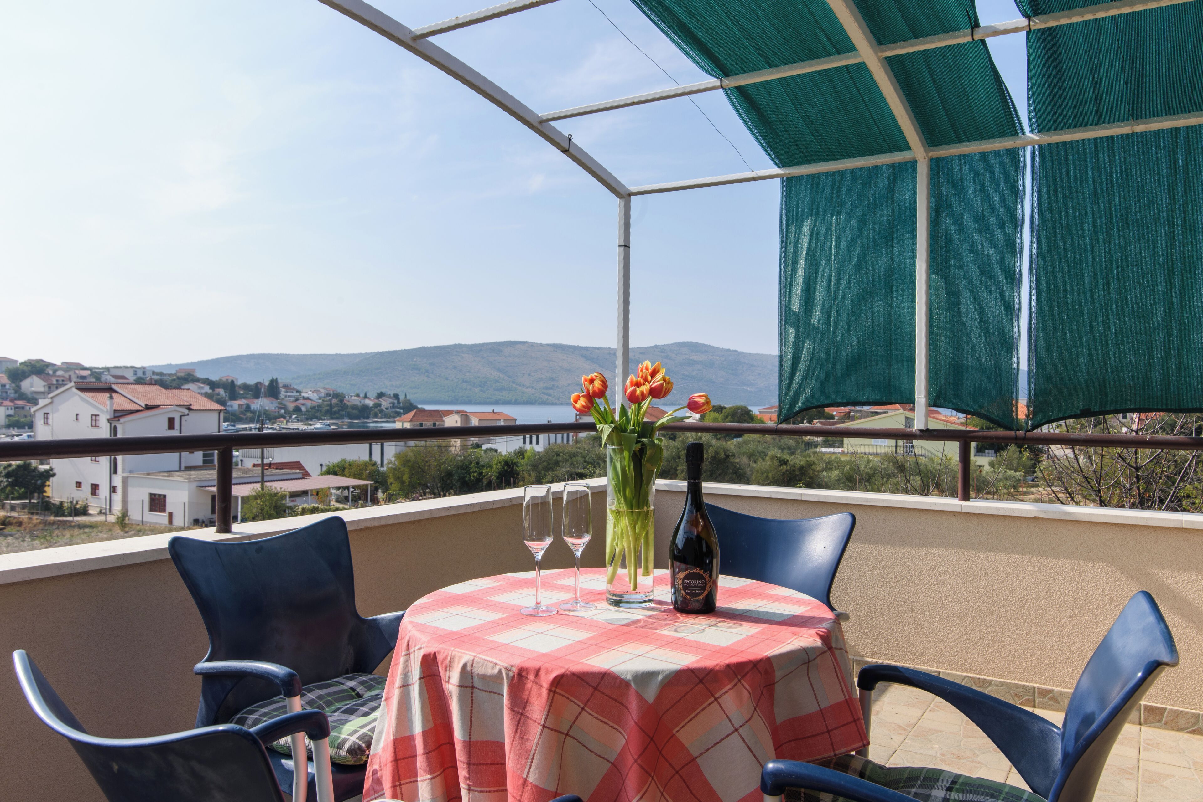 Un balcon avec une table dressée pour deux personnes, une bouteille de vin et un vase rempli de fleurs.