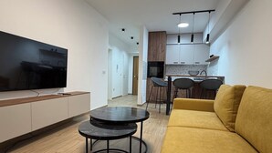 A modern living room with a sofa, a TV, and a dining area with chairs and a table. - Sky 47 apartment - modern comfort with free parking (Ohrid)