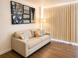 A living room with a beige sofa, colorful pillows, and abstract art on the wall. - @ Marbella Lane - King Studio Steps to Beach Oasis (Honolulu)
