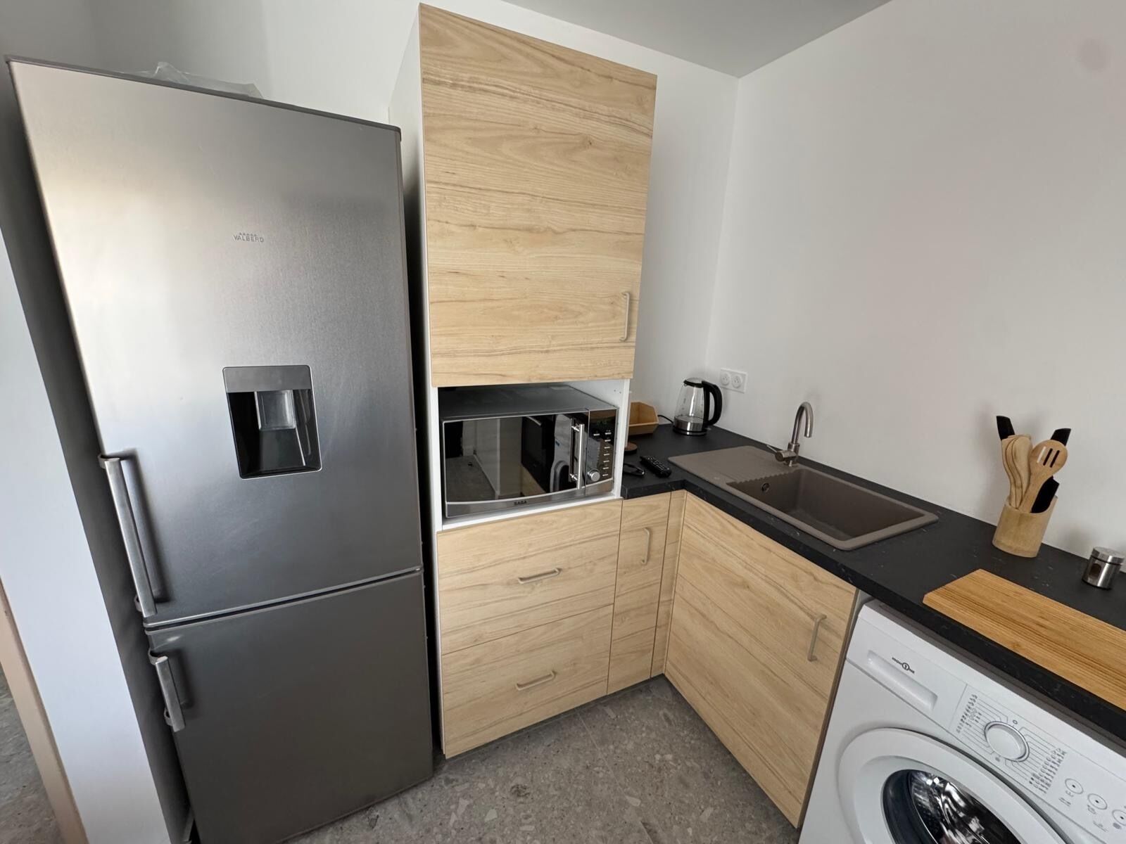 Eine kompakte Küche mit Edelstahlkühlschrank, Mikrowelle, Spüle und Waschmaschine.