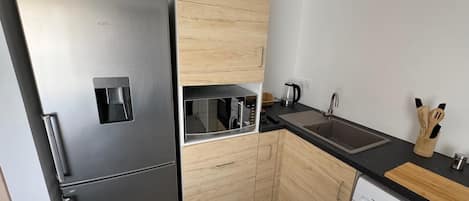 A compact kitchen with a stainless steel refrigerator, a microwave, a sink, and a washing machine.