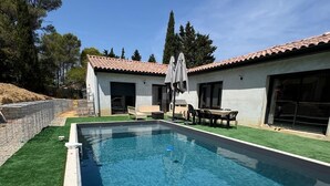 A swimming pool with a tiled deck, surrounded by a grassy area and a building with a tiled roof.