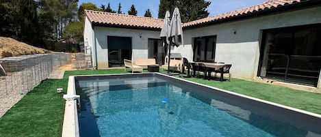 A swimming pool with a tiled deck, surrounded by a grassy area and a building with a tiled roof.