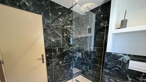 A modern bathroom with a glass-enclosed shower, marble walls, and a white toilet.