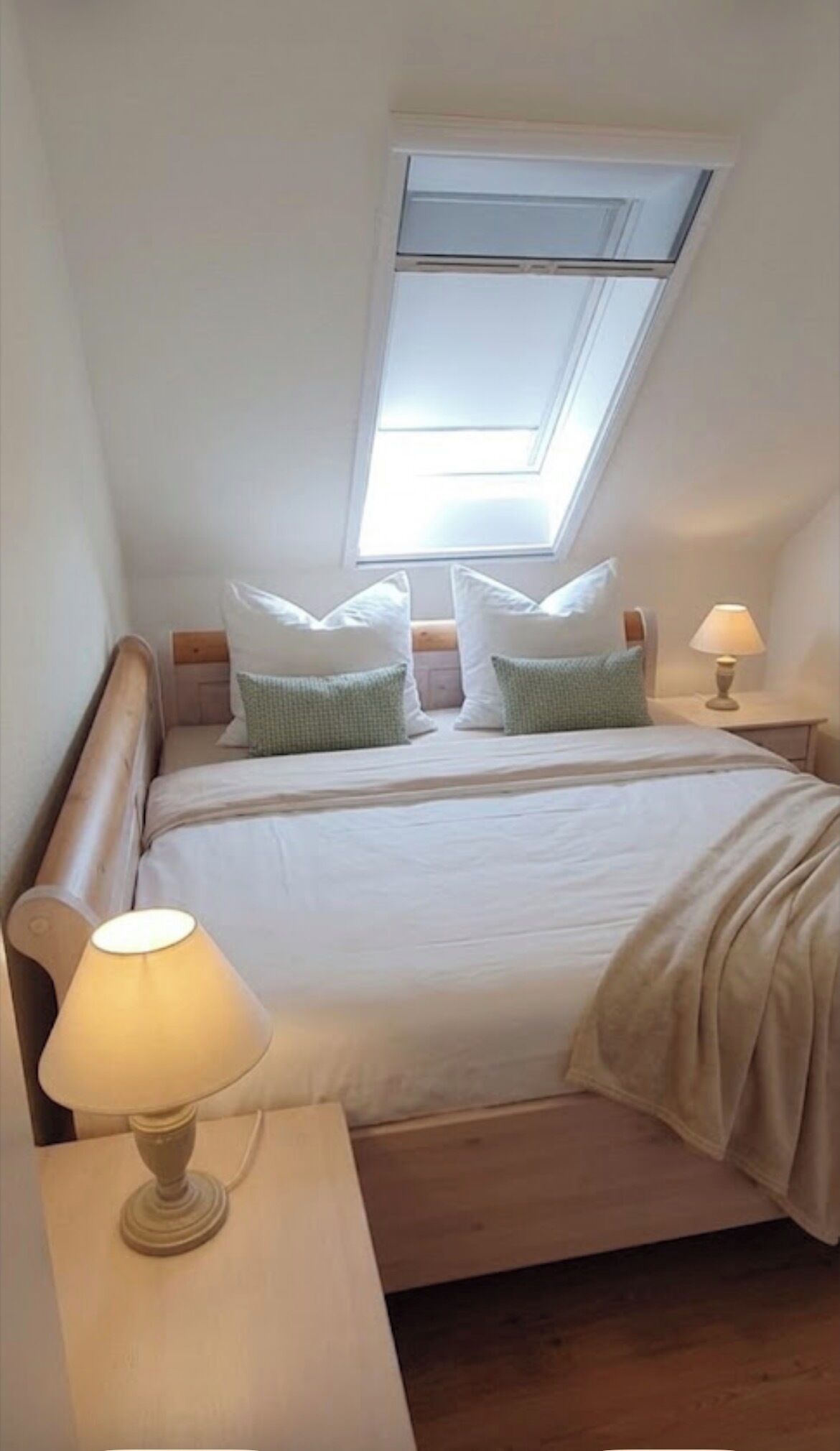 A bedroom with a skylight, a bed with pillows, a bedside lamp, and a nightstand.
