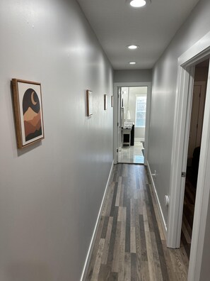 A hallway with a wooden floor, white walls, and a framed picture on the left.