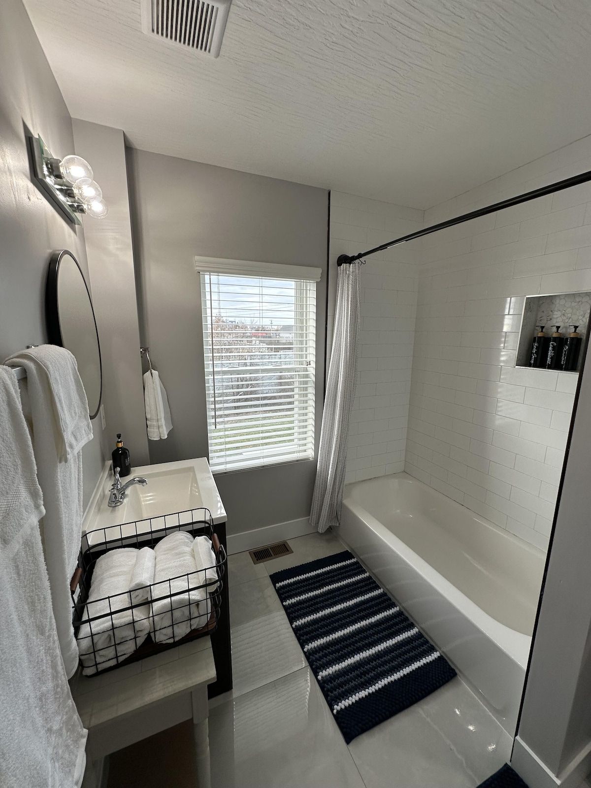 A modern bathroom with a bathtub, a sink, a mirror, and a window with blinds.