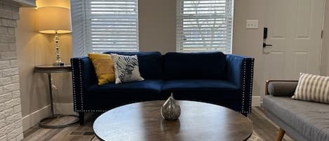 Un salon avec un canapé bleu foncé, une table basse ronde et une lampe sur une table d’appoint.