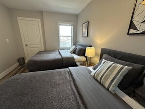 A hotel room with two beds, a window, a door, and a lamp.